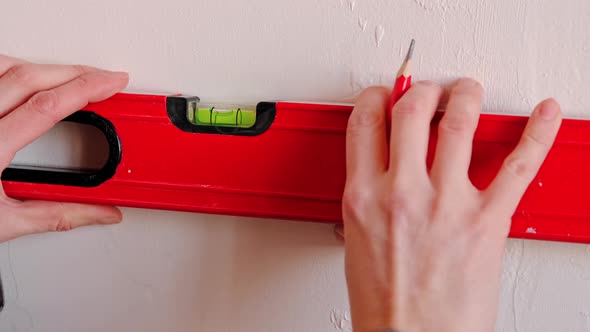 Drawing horizontal markings on the wall by level - DIY home repair. A woman in a red baseball cap an