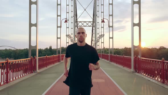 Young Man in Black Sports Uniform Runs on the Pedestrian Bridge at Dawn