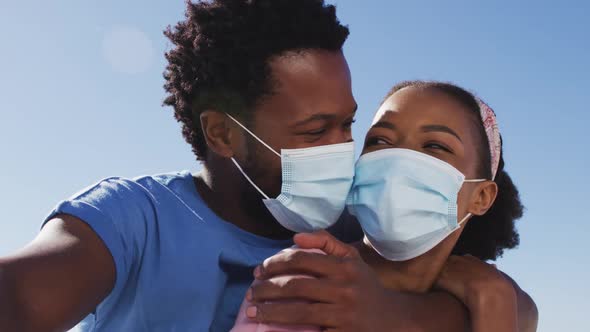 Portrait of african american couple wearing face masks looking to camera on the beach