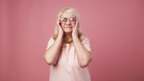 Tired Senior Woman Suffering From Headache Massaging Her Temples and Grabbing Head Pink Background