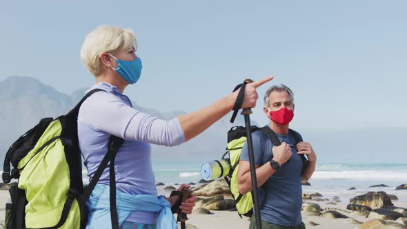 Senior hiker couple wearing face masks with backpacks and hiking poles pointing towards a direction 