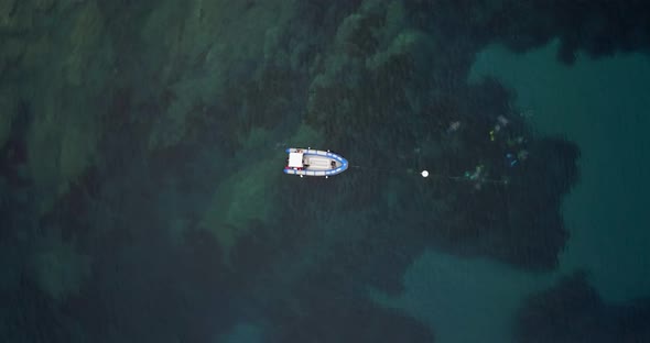 Several divers diving submerged next to a small boat aerial view from drone