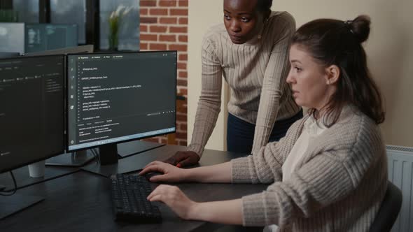 Junior Developer Writing Source Code Under Senior Dev Supervision Sitting at Desk with Multiple