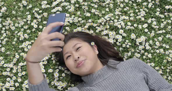 Happy asian girl taking a selfie with a daisy between her hair and daisies co