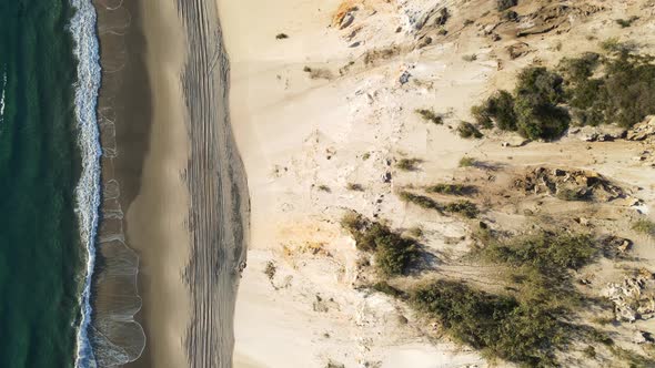 Drone view looking down following along a 4wd drive beach road next to the ocean and steep cliff fac