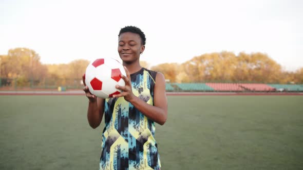 A Serious Young Black Girl in a Sleeveless Tshirt Stands on a Soccer Field and Holds a Ball in Her