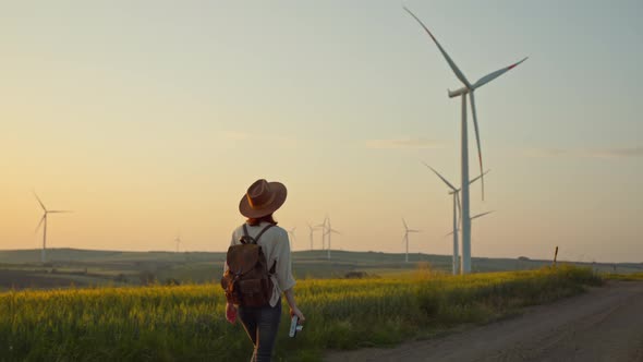 Young photographer walking near a farm with alternative green energy windmills at sunset