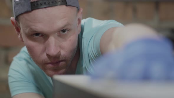 Close Up Face of the Concentrated Man in the Cap, Involved in His Work. The Gloved Worker Checking