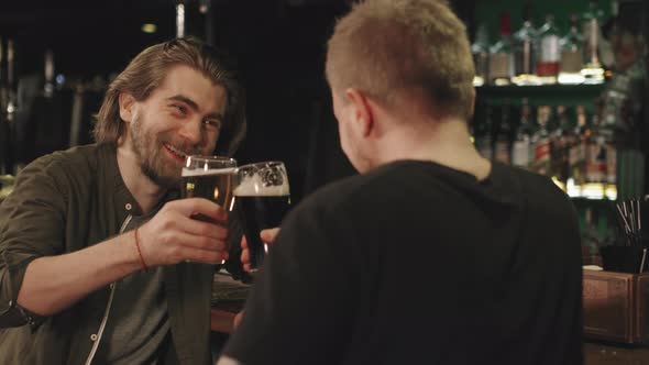 Happy Men Toasting Beer Mugs At Bar