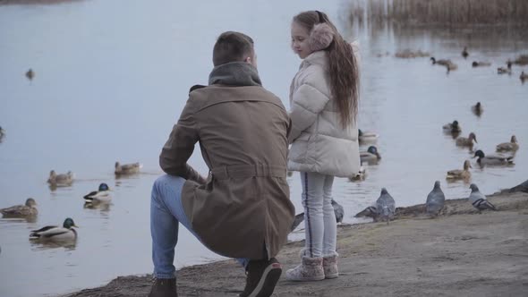 Wide Shot Portrait of Pretty Brunette Girl Talking with Young Father on Riverbank. Caucasian Child