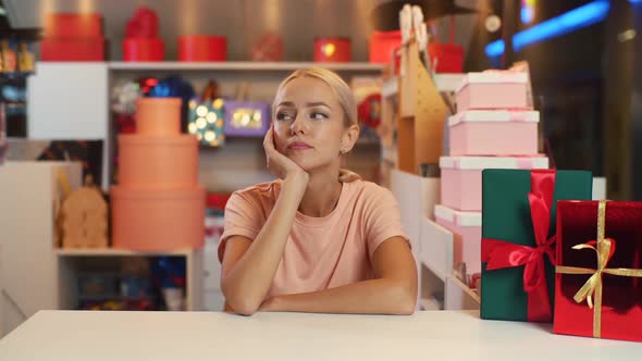 Portrait of Sad Attractive Young Sales Woman Sits at Counter of Holiday Store in Mall Waiting for