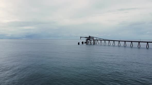 Old abandon coal loading dock protruding out above a moody sky ocean. Moving drone view