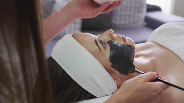 Caucasian woman lying back while beautician gives her a face mask