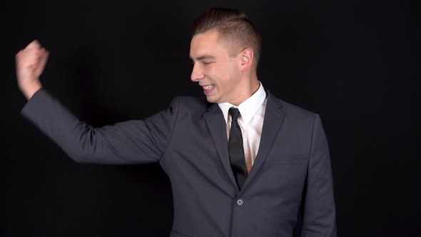 Young Businessman Shows Biceps on His Arm. Man in a Black Suit on a Black Background