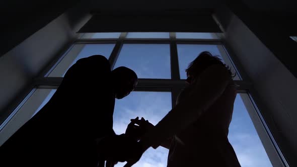 Two Dark Silhouettes Against the Window. a Man and a Woman Dance. Bottom View