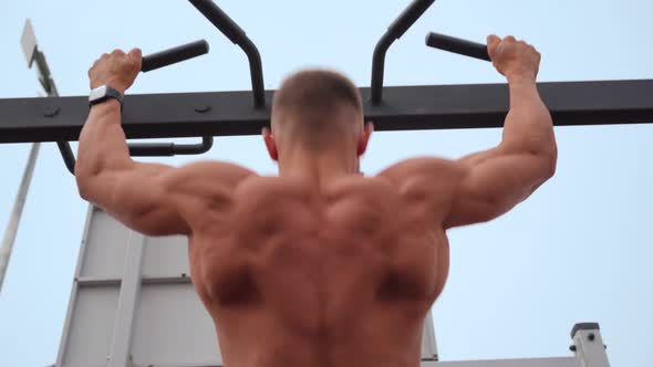 Athletic Man Pumps Up Muscles Doing PullUps Open Sports Ground with Bare Torso