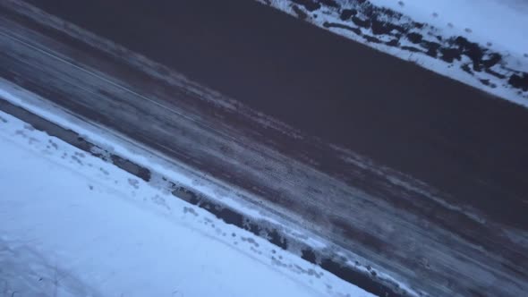 Rising top-down aerial footage over a road surrounded by snow and trees.