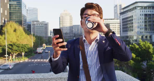 Asian man drinking coffee and using smartphone while sitting on the roof of corporate park