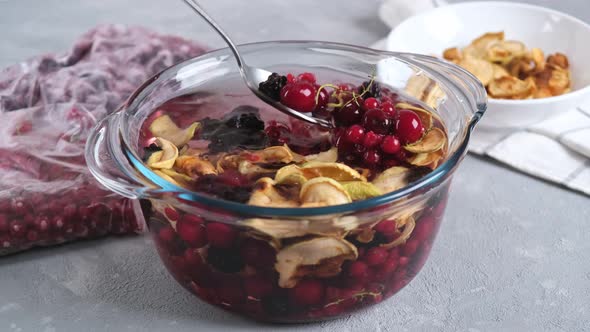 Cooking homemade healthy drink or compote from dried apples and frozen berries on a light background