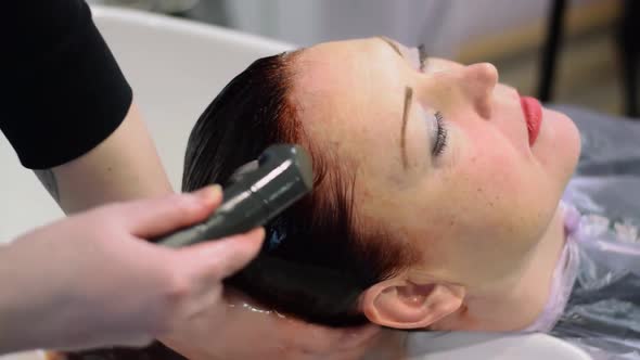 Hairdresser is washing the long red hair of the middle-aged woman