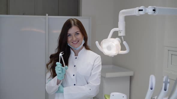 Happy Dentist in Uniform Shows Dental Tool at Camera and Smiles in Clinic