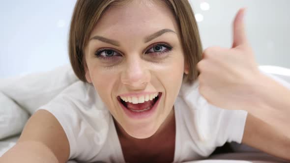 Thumbs Up by Happy Woman Lying in Bed on Stomach