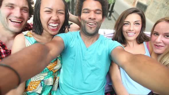 Five young adults laughing while taking a group selfie