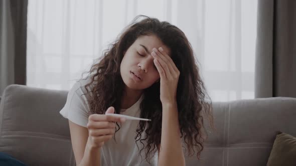 Sick Young African American Woman Checking Body Temperature Holding and Looking at Thermometer