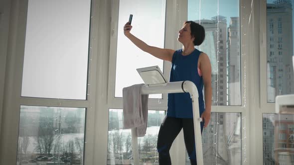 Slim fit female athlete is taking selfie on treadmill. Home fitness activity