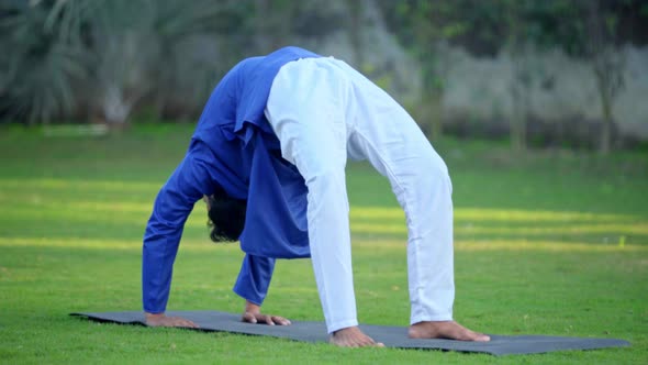 Indian man doing a Wheel Yoga pose or Chakrasana in a park