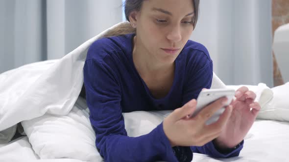 Hispanic Woman Lying in Bed Using Phone for Browsing Online