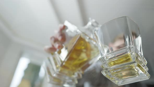 Shooting Under Glass Table of Blurred Man Pouring Whiskey From Decanter in Glass and Taking Drink in