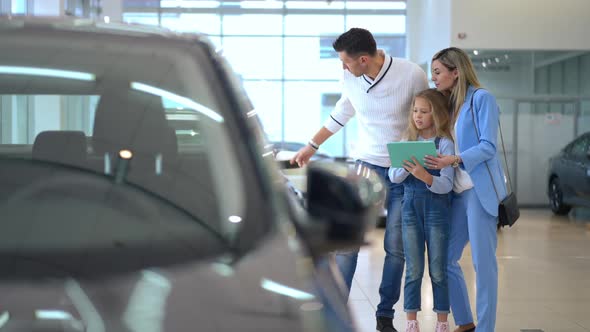 Wide Shot Curios Daughter Talking with Father and Mother Choosing New Vehicle in Car Dealership