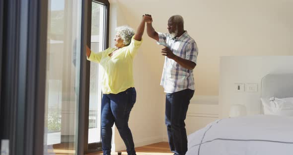 Happy senior diverse couple dancing in living room at retirement home