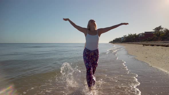 Mature woman in sarong and tank top throws her arms up rejoicing in her freedom, splashing in the wa