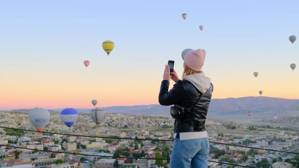 Happy Slim Sexy Woman in Tight Jeans Looks at Sunrise with Balloons and Takes Pictures of This