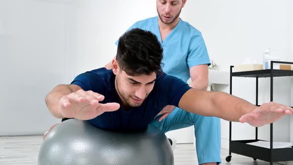 Physiotherapist Helps Handsome Young Patient for Doing Pilates Exercises with Ball