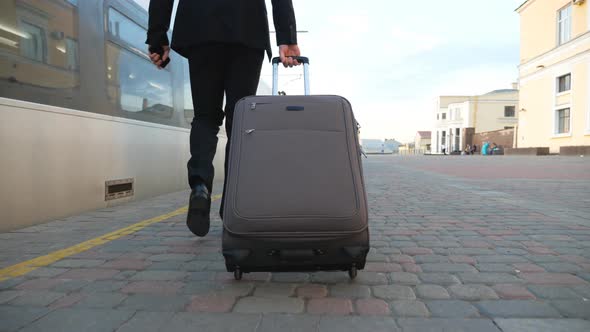 Legs of Successful Businessman in Suit Walking Along Platform and Pulling Suitcase on Wheels. Young