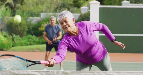 Video of happy biracial senior woman practicing tennis on tennis court