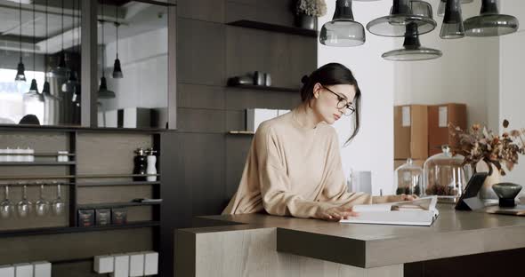 Attractive Motivated Female in Eyeglasses Enjoy in Kitchen Room and Read a Book