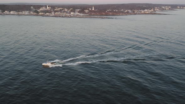 Fishing boat heading out at sunrise with two lighthouses in the distance AERIAL