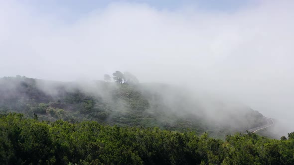 Flying Through the Clouds Over a Mountain Landscape and Road Surrounded By Green Vegetation