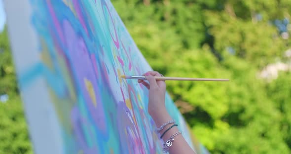 Close up of a woman's hand painting on a big canvas on a summer afternoon