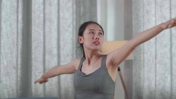 Asian Athletic Female Exercising, Stretching And Practicing Yoga In Warrior Ii Pose At Home