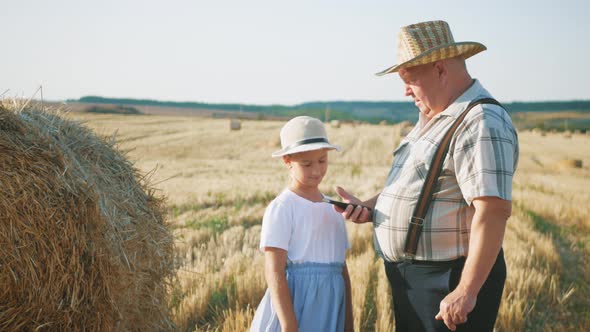 Little Girl with Grandfather in Field Haystacks, Grandfather Farmer Is Teaching the Younger