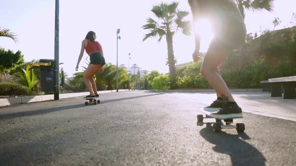 Two Female Friends on Skateboards Rides Downhill at the Resort Having Fun Moving and Smiling. Road
