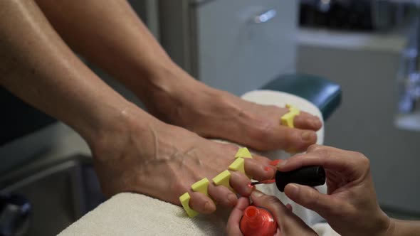 With toe spacers in place, pedicurist paints toenails with red polish.  Camera slide from left to ri