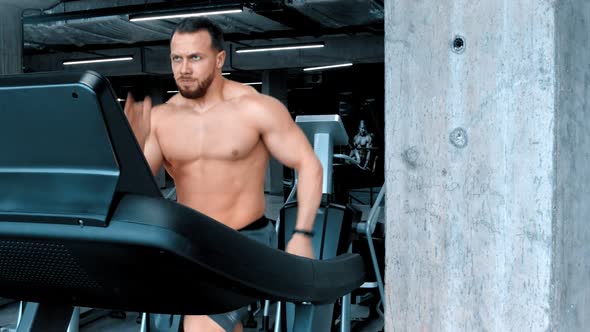 A Bearded Attractive Young Man Bodybuilder Running on the Treadmill with an Effort in the Modern Gym