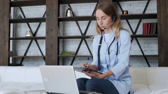 Woman Wears a White Coat and a Headset While Talking on a Laptop Computer Using an Online Video Call