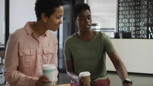 Two happy diverse businesswomen with coffee working together in office